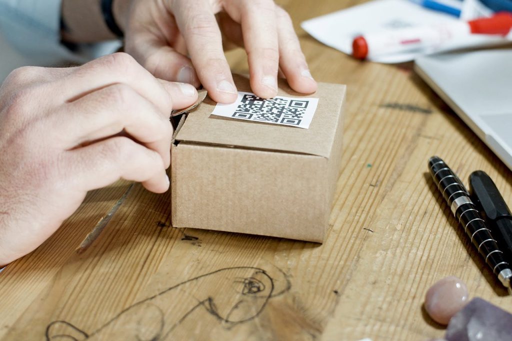pexels-photo-7289721 Close-up of hands packing a box with a QR code, symbolizing online business services.